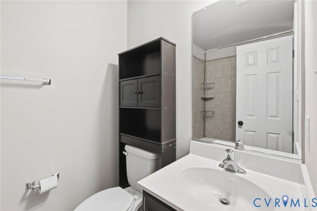 Built-in dark wood-finish storage cabinetry, single vanity with integrated sink, chrome-finish faucet, and tiled shower surround