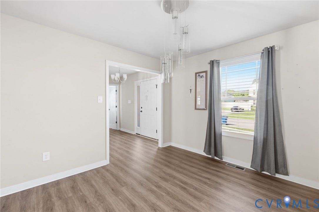 Spacious room with wood-finish flooring, neutral wall paint, a modern chandelier, and a large window