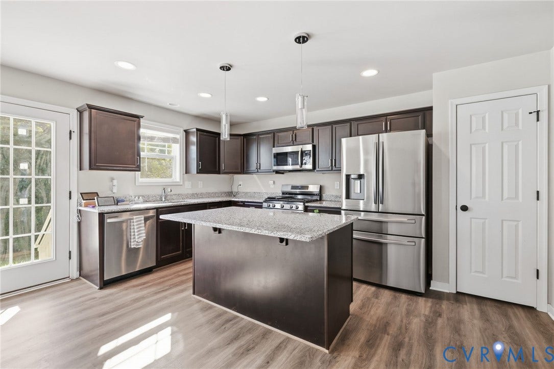 Kitchen featuring wood-finish flooring, dark wood cabinetry, stainless steel appliances, a center island with a stone countertop, and recessed lighting
