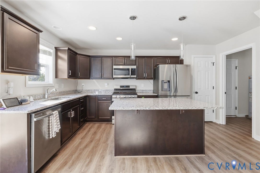 Kitchen featuring dark wood-finish cabinetry, light speckled countertops, stainless steel appliances, a center island with pendant lighting, and wood-finish flooring