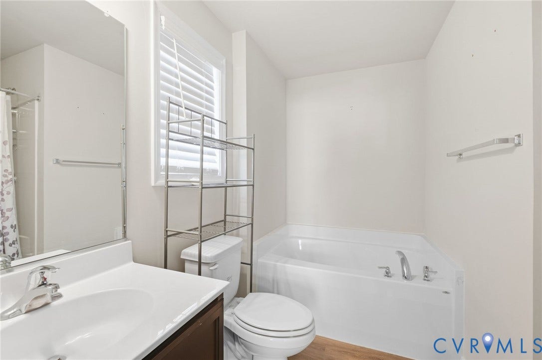 White bathtub with chrome fixtures, wood-finish flooring, white vanity with integrated sink, chrome faucet, and a window with white blinds