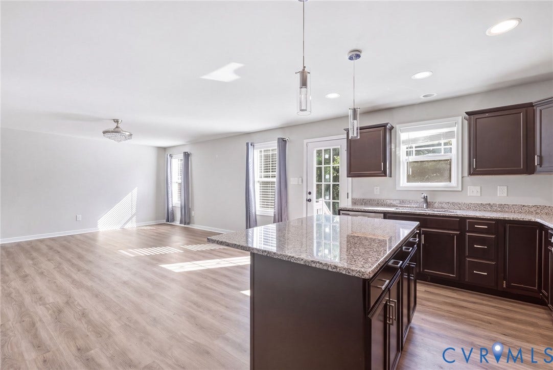 Open-concept living area featuring wood-finish flooring, recessed lighting, and a kitchen island with stone countertops