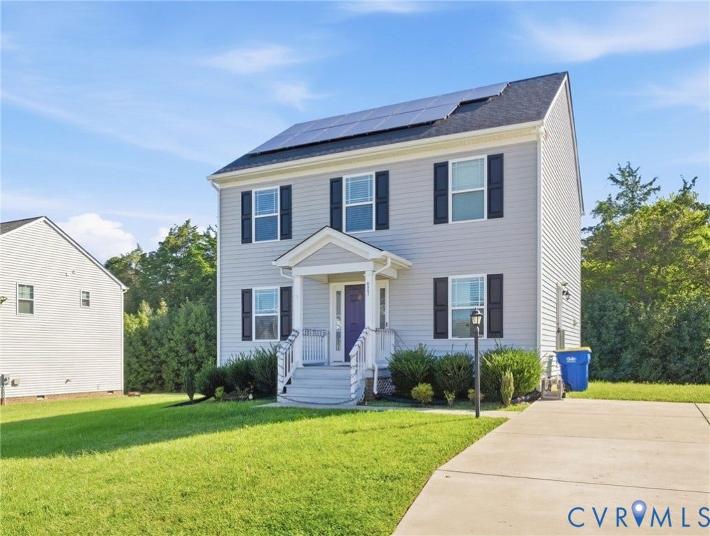Two-story residence featuring light gray siding with black shutters, solar panels, and a concrete driveway