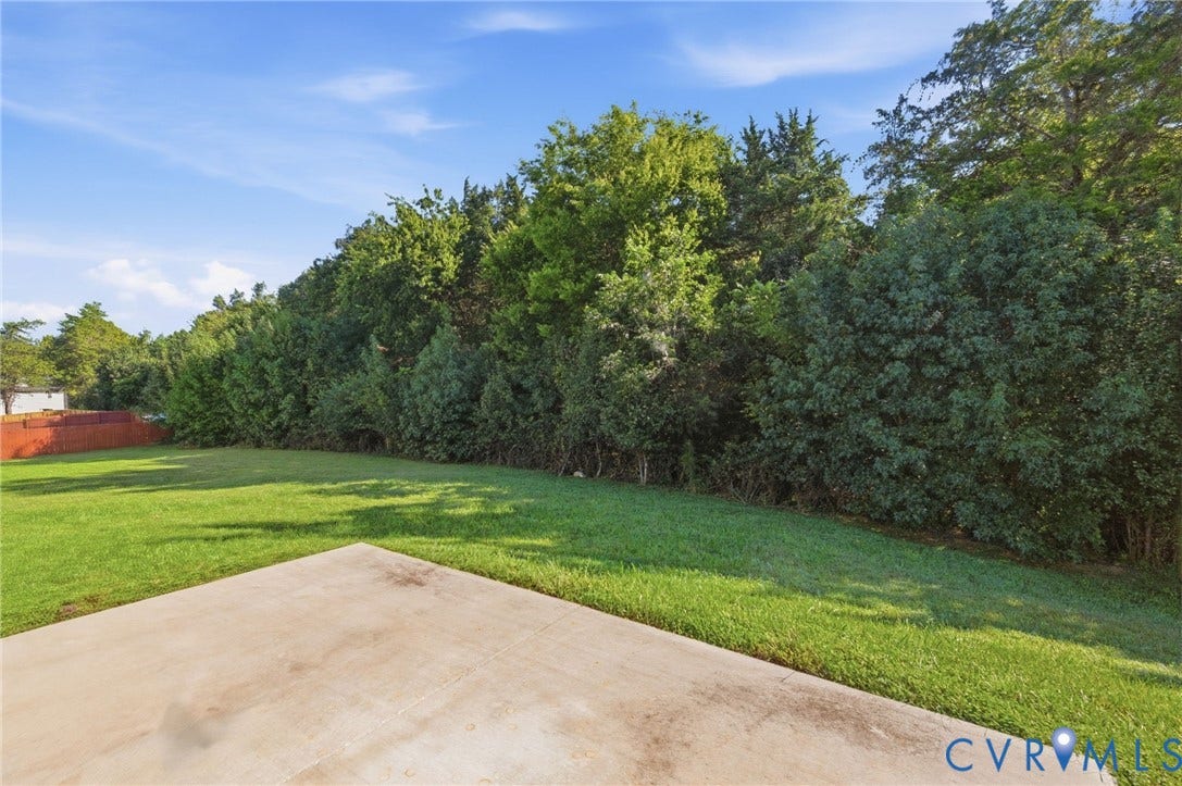 Expansive backyard featuring a lush lawn, concrete patio, and a privacy fence