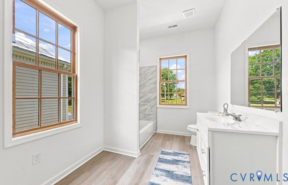 104 E Fillmore Street, Petersburg, VA 23803 Wood-finish flooring, white vanity with integrated sink, rectangular mirror, and a tub with tiled surround