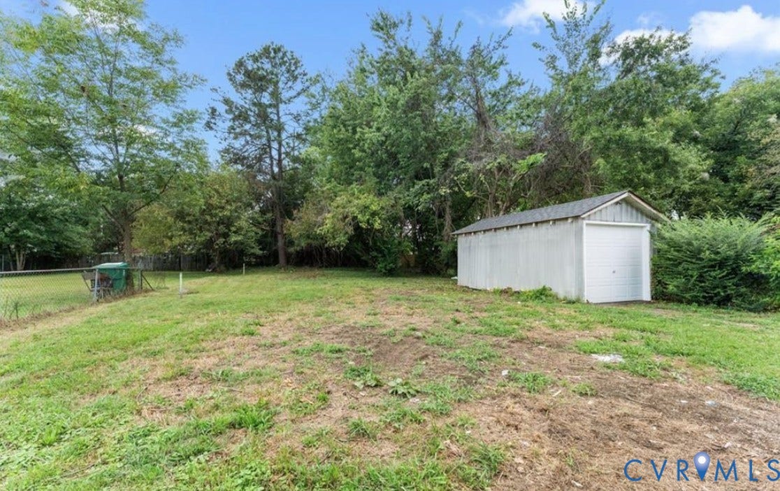 222 Elm Street, Petersburg, VA 23803 Expansive grassy area with a chain-link fence, mature trees, and a detached storage shed