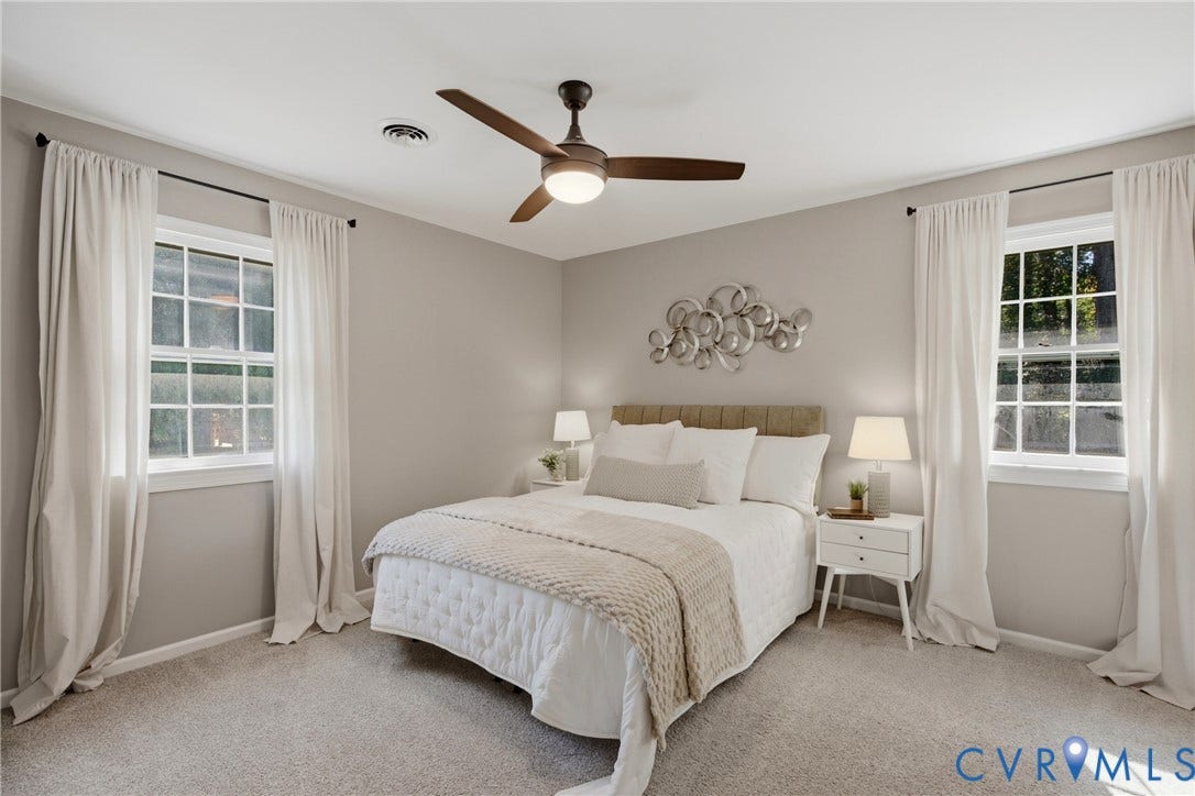 Light gray wall paint, carpeted flooring, two double-hung windows, and a ceiling fan with integrated lighting