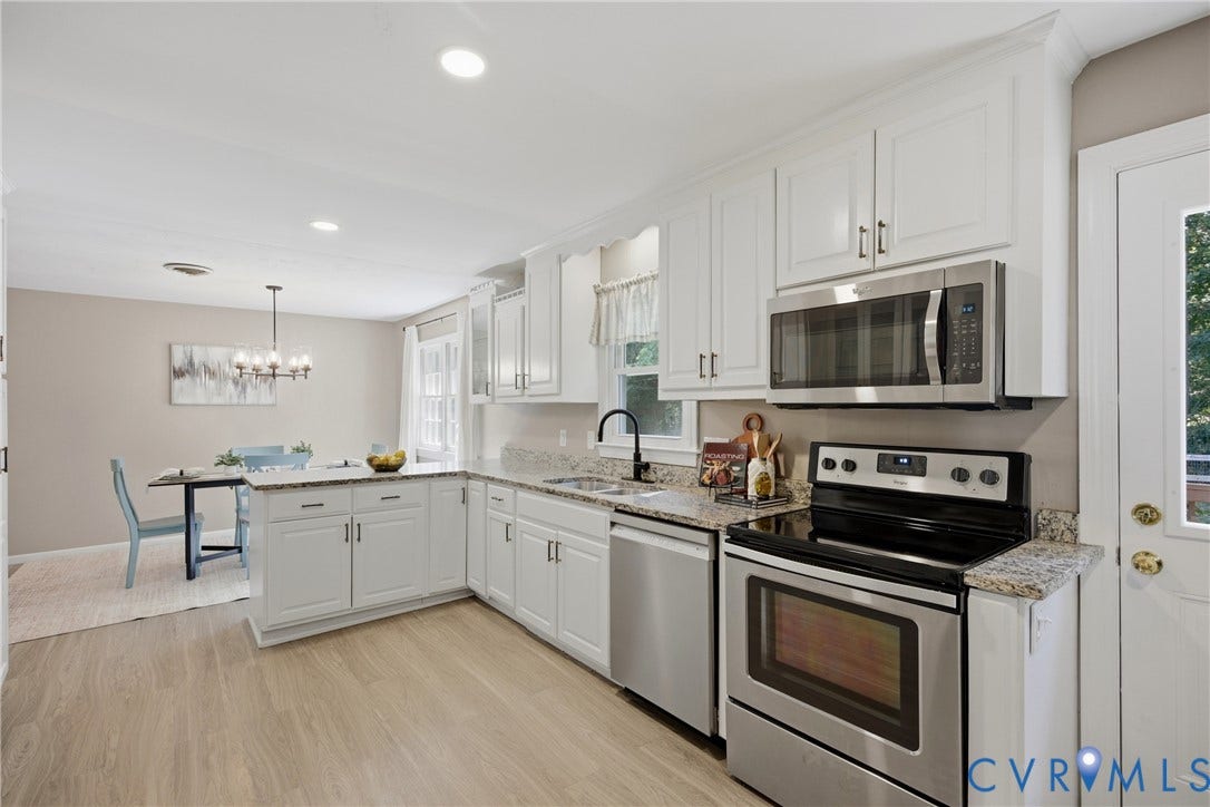 Open-concept kitchen with white cabinetry, stainless steel appliances, granite countertops, and wood-finish flooring