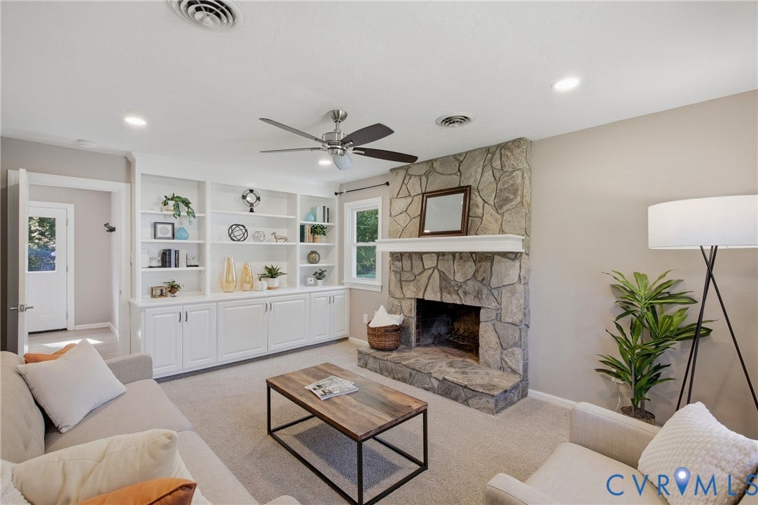 Bright, open living room anchored by a striking stone fireplace with mantel and hearth, complemented by extensive white built-in cabinetry with shelving and storage