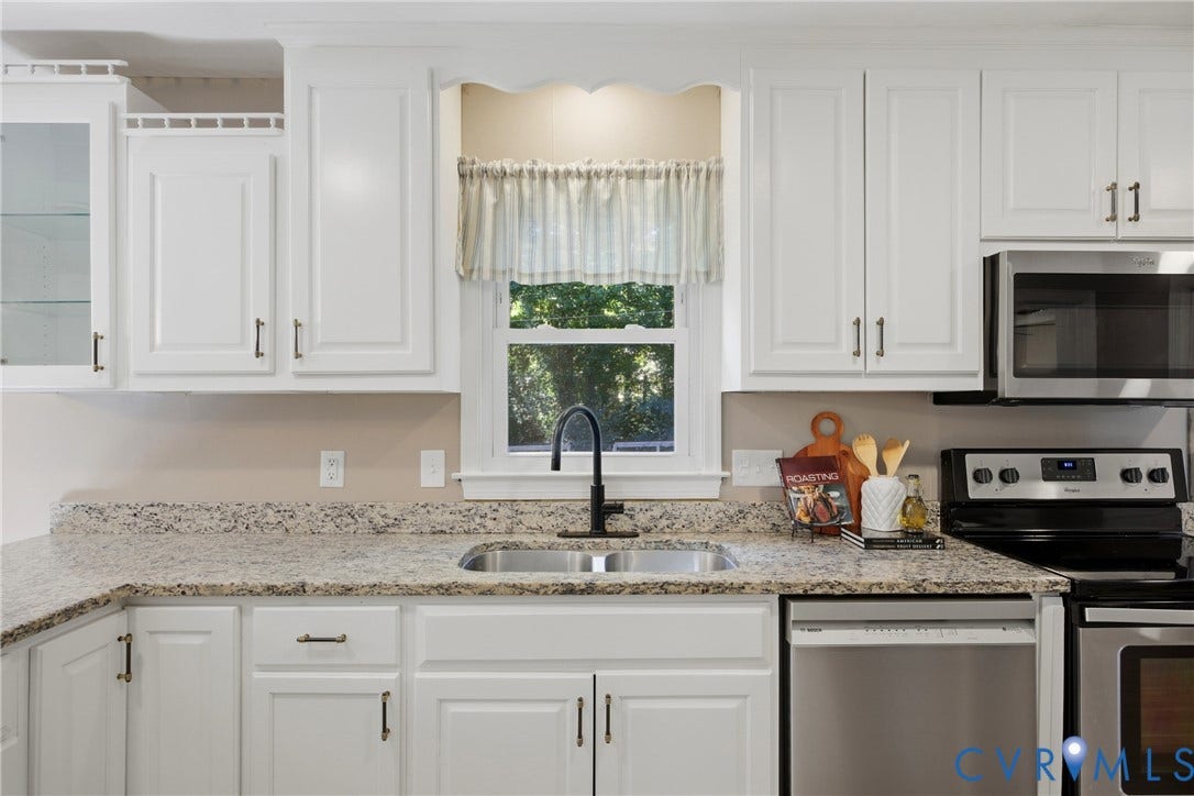 White cabinetry with dark hardware, stone-finish countertops, stainless steel appliances, and a double basin sink with a gooseneck faucet