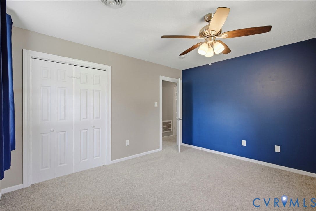 Plush carpet flooring, a ceiling fan with integrated lighting, bi-fold closet doors, and contrasting accent wall