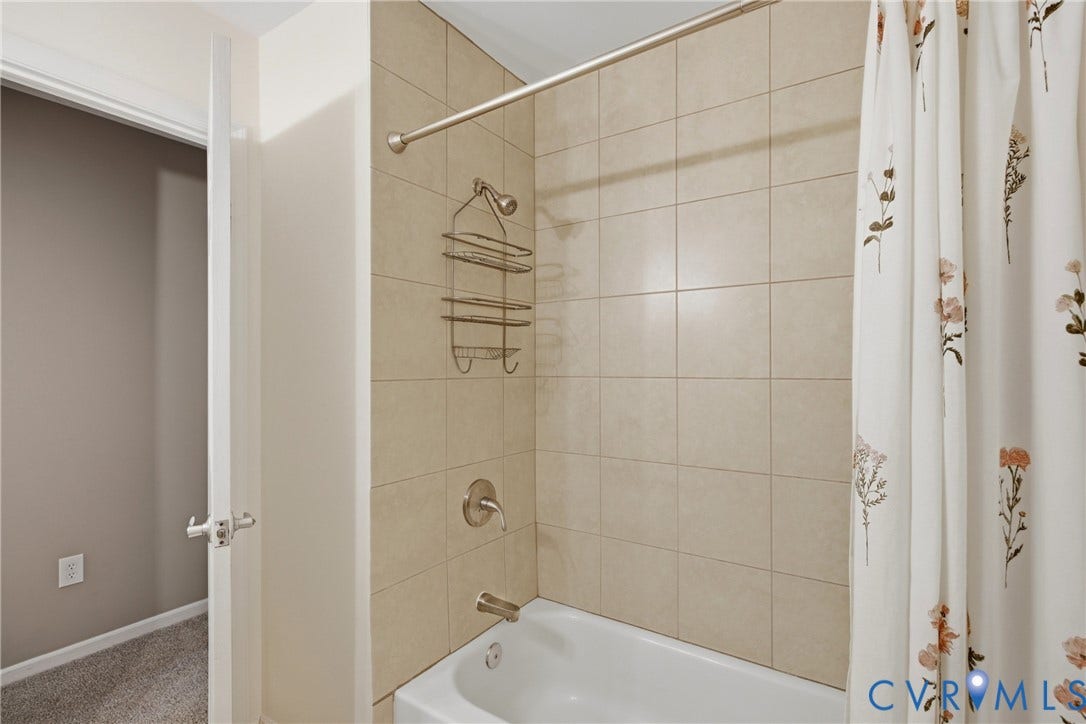 Bathtub with tile surround, brushed nickel fixtures, and a curved shower rod