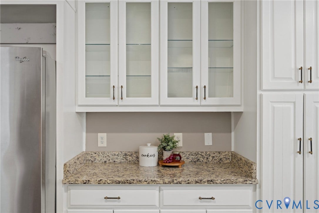 White cabinetry with glass-front upper cabinets, light-colored speckled countertop, and brushed bronze hardware