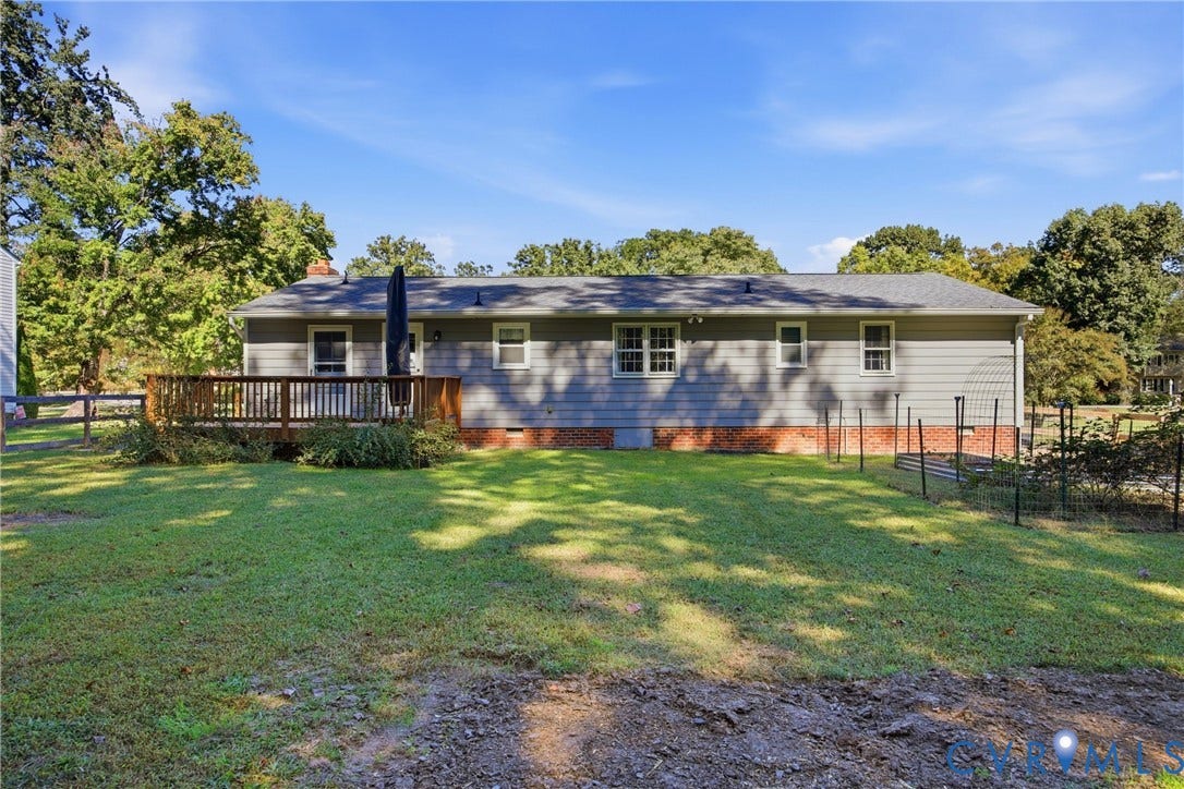 Expansive backyard featuring a wood deck, gray siding, and a brick foundation