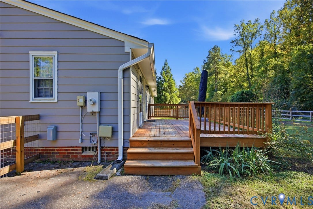 Wood deck with railing and steps, gray siding exterior, brick foundation, and mature trees
