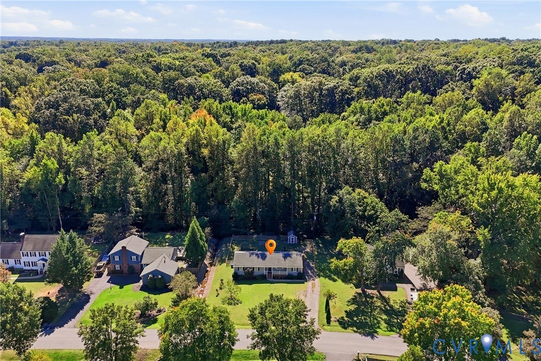 Ranch-style residence featuring a prominent front porch, expansive front lawn, paved driveway, and mature landscaping