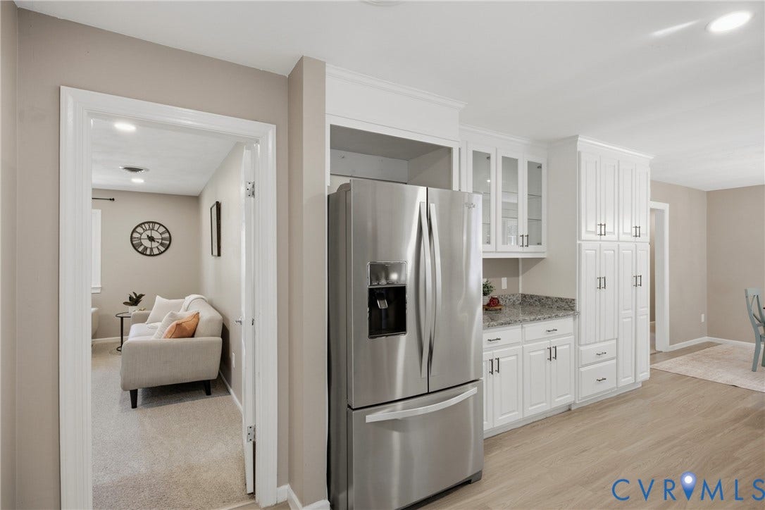 White cabinetry with dark hardware, stainless steel refrigerator, stone-finish countertops, wood-finish flooring, and recessed ceiling lighting