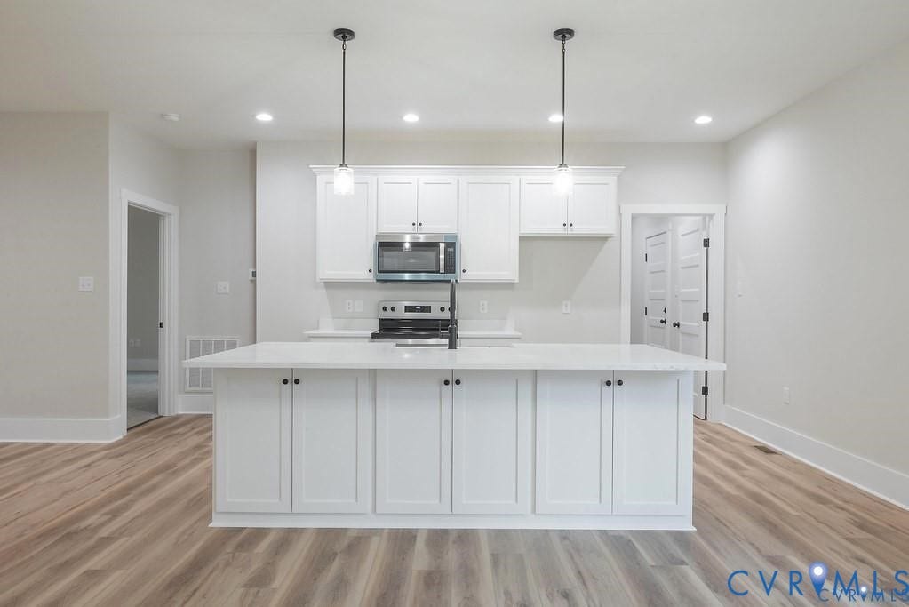 5301 Chimney Springs Drive, Goochland, VA 23063 Kitchen featuring an expansive island with white cabinetry, pendant lighting, stainless steel microwave, and wood-finish flooring