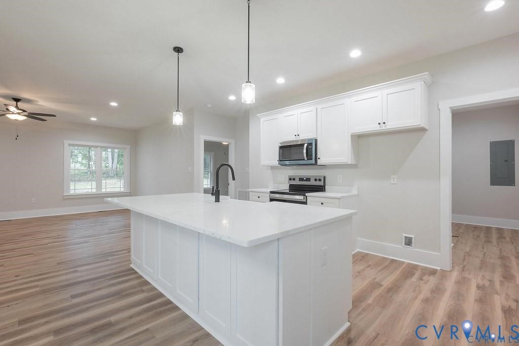 5301 Chimney Springs Drive, Goochland, VA 23063 Kitchen island with a white countertop and dark-finish faucet, recessed lighting, wood-finish flooring, and white cabinetry with dark hardware