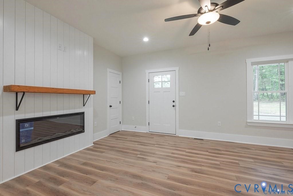 5301 Chimney Springs Drive, Goochland, VA 23063 Living space featuring wood-finish flooring, a wall-mounted electric fireplace with a wood mantle, a ceiling fan, and a paneled entry door