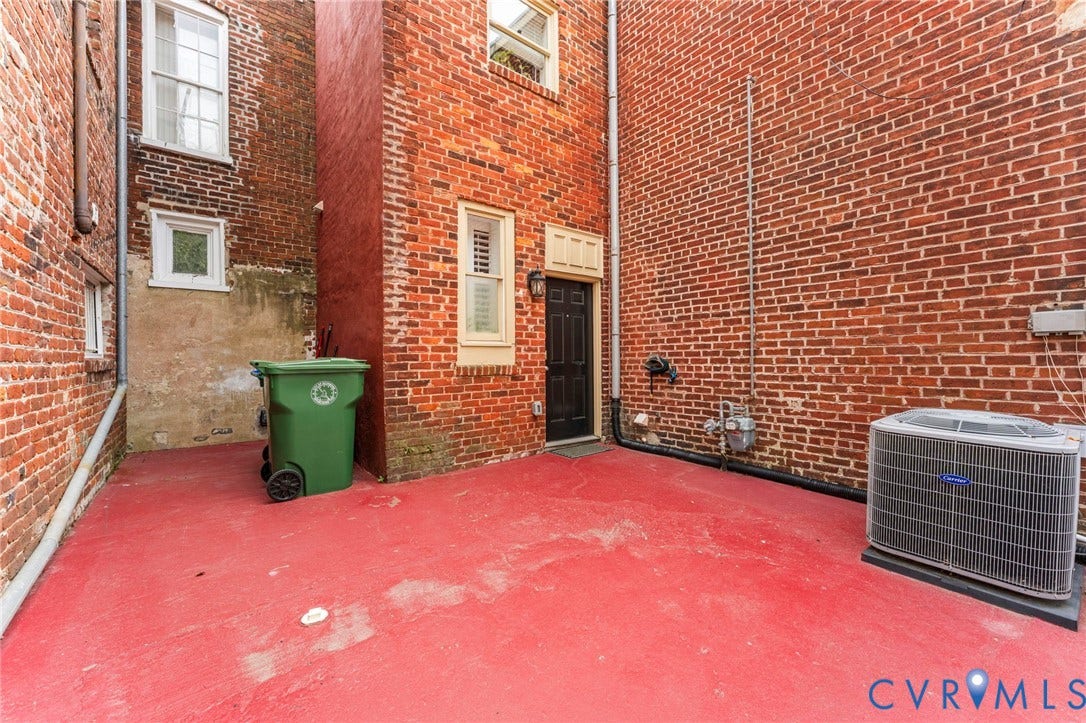 Red-painted concrete patio with brick exterior walls, a dark-colored entry door, and an exterior HVAC unit
