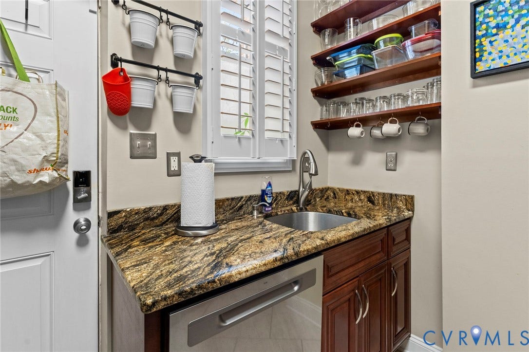 Custom cabinetry with a rich wood finish, granite countertop, undermount stainless steel sink, and stainless steel dishwasher