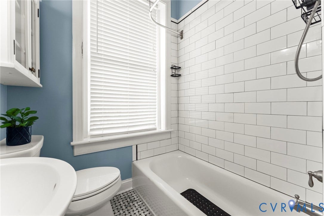 White subway tile bath surround, built-in tub with shower fixture, and a window with blinds