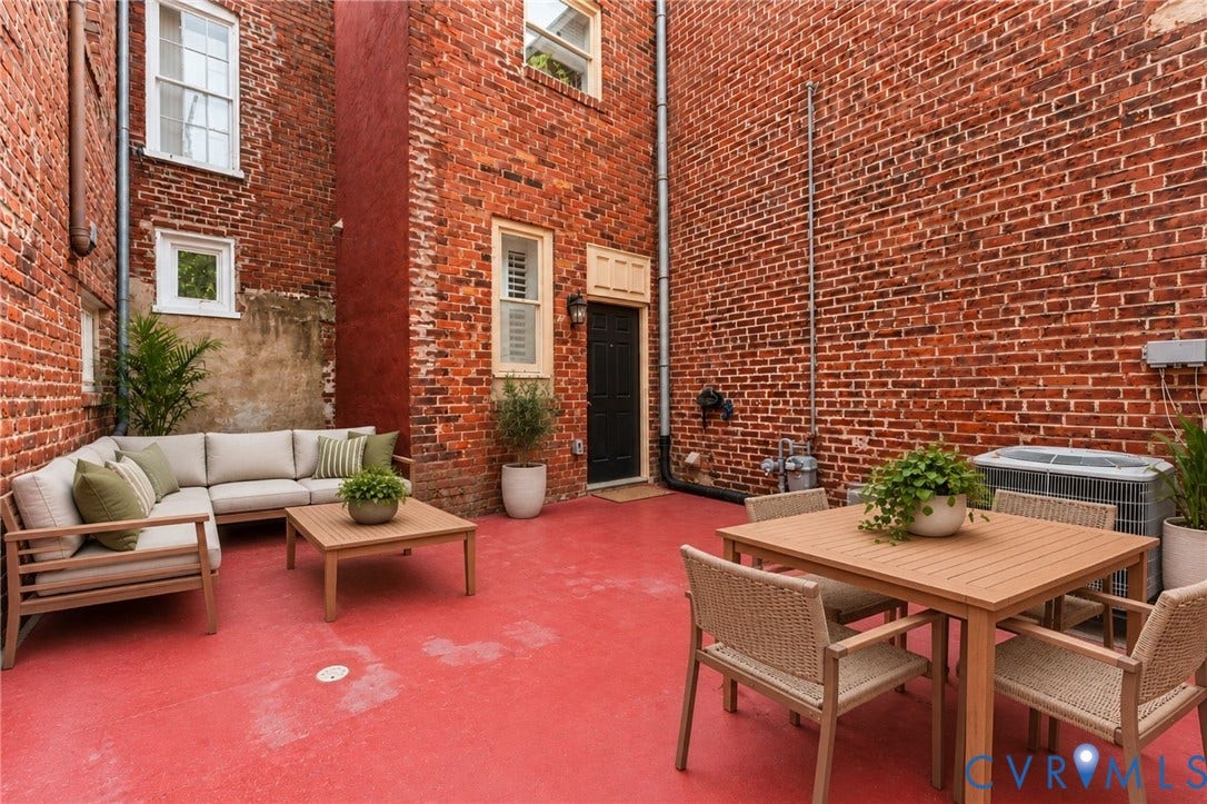 Brick exterior featuring a red-hued patio surface, multiple window openings, and a dark-colored entry door