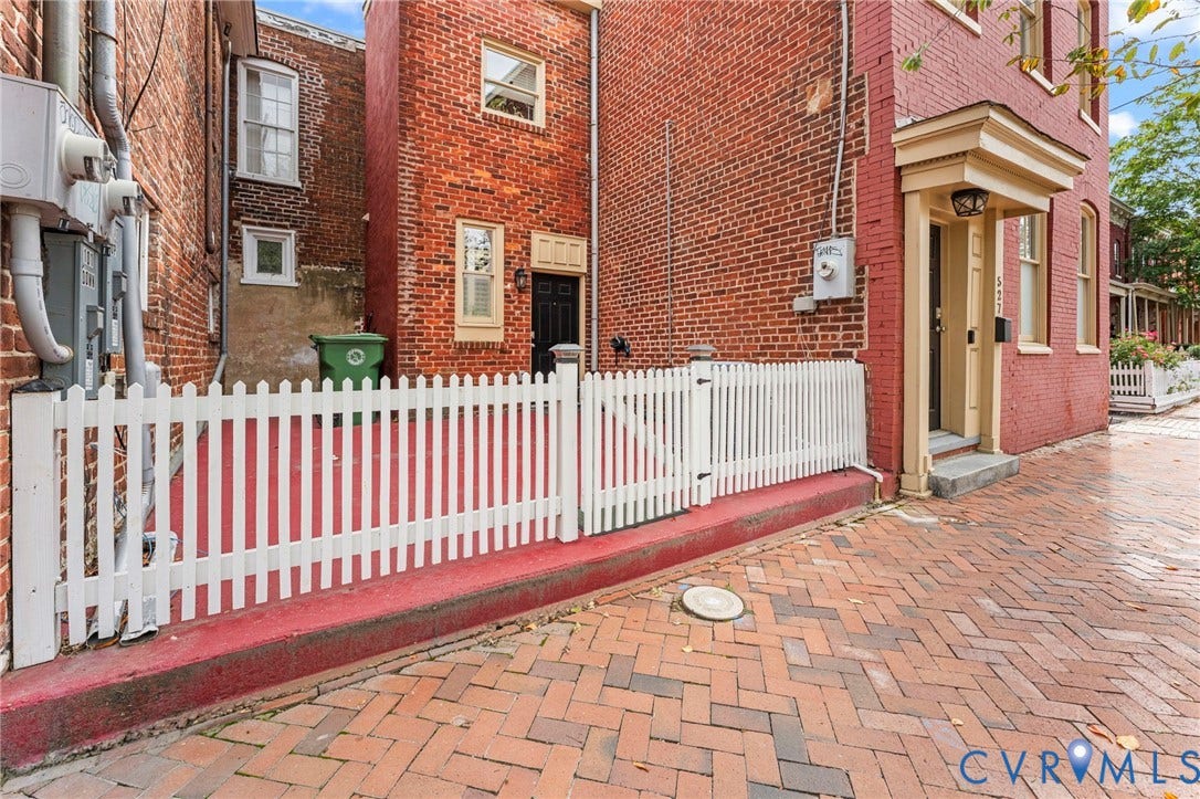 Brick exterior with white picket fencing, an ornate entry door surround, and herringbone brick paving