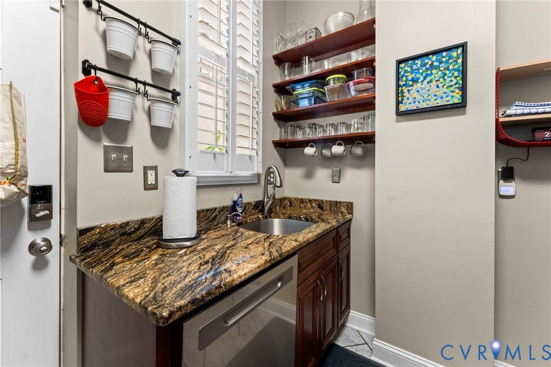 Built-in bar area featuring rich wood cabinetry, patterned stone countertop, and an undermount stainless steel sink