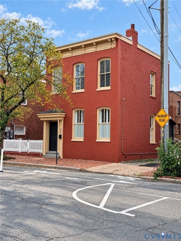Brick exterior featuring a detailed cornice, multiple windows with shutters, a prominent front door with an overhang, and a brick sidewalk