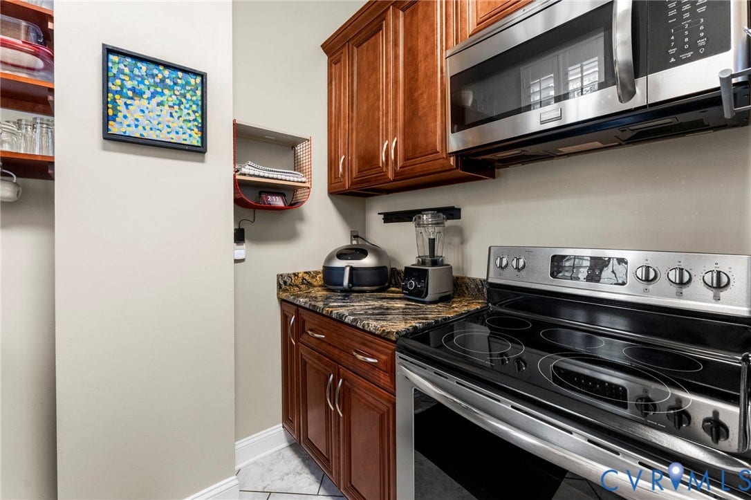Stainless steel microwave, electric range with glass cooktop, wood-finish cabinetry, and granite-style countertop