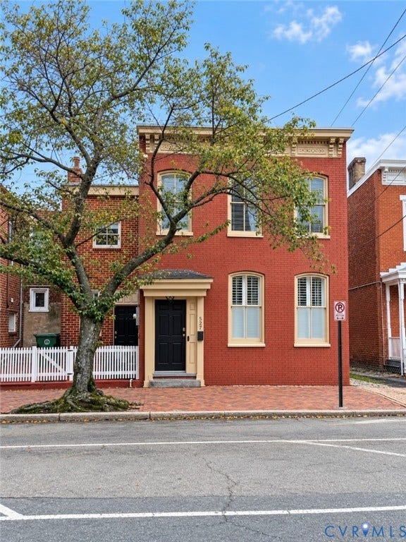Brick facade with decorative cornice, white shuttered windows, and a portico entry