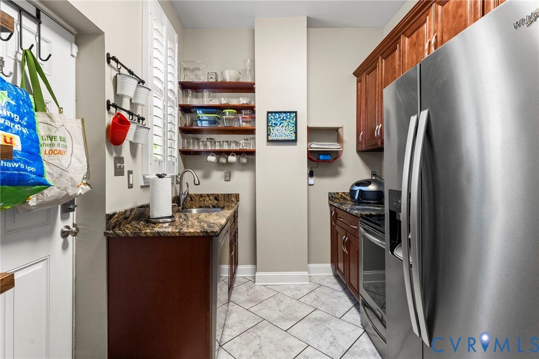 Stainless steel refrigerator, wood-finish cabinetry, patterned stone countertop, single basin sink, and white tile flooring