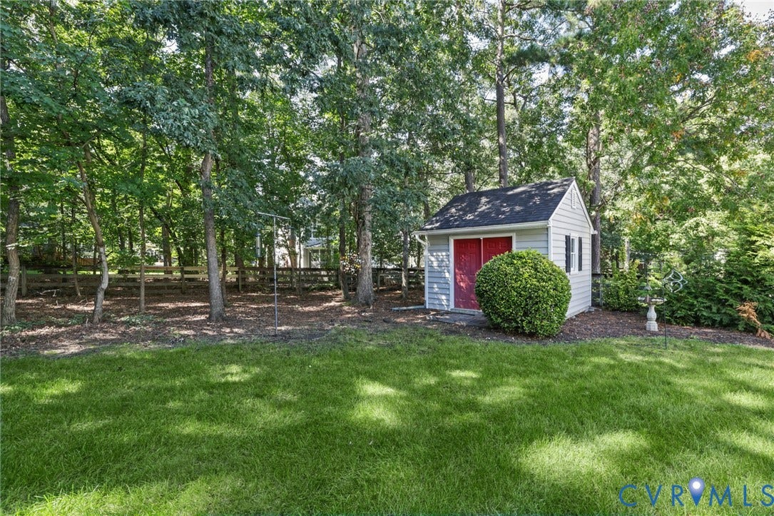 Expansive backyard featuring a manicured lawn, storage shed with red doors, and a natural tree line