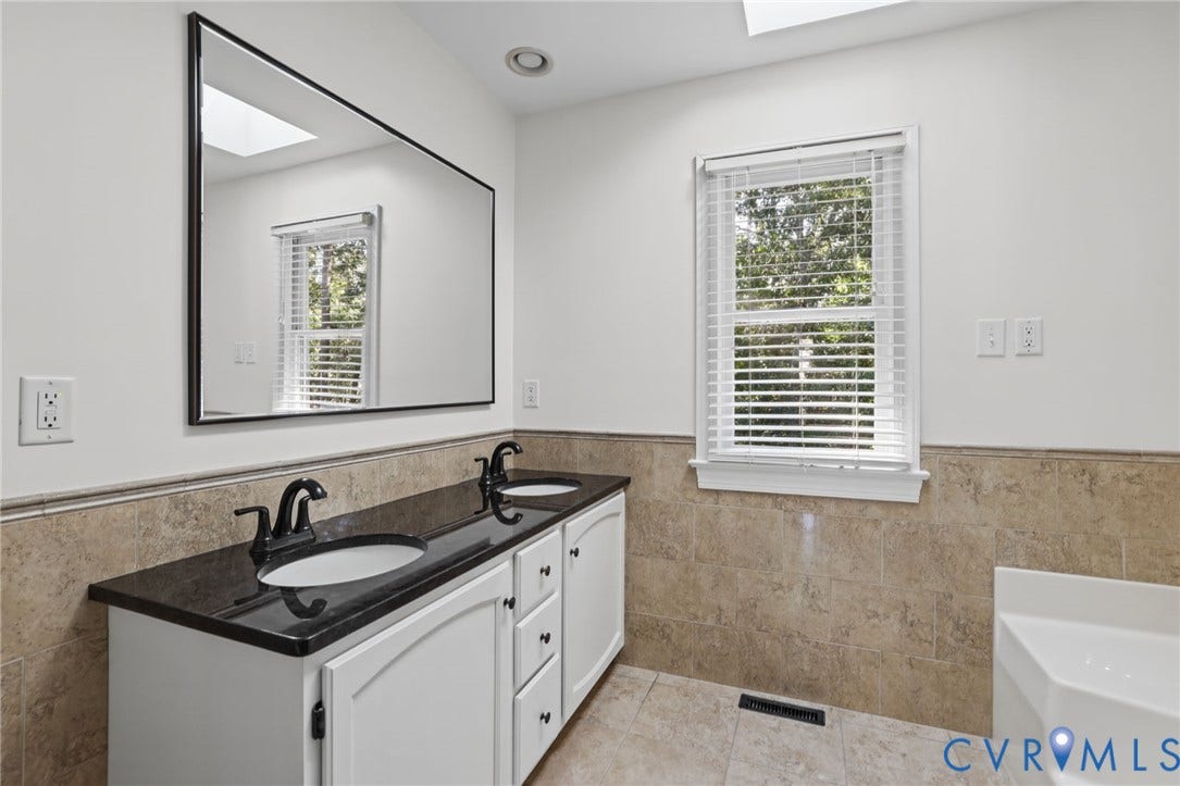 Dual vanity with black countertop, white cabinetry, and matte black fixtures