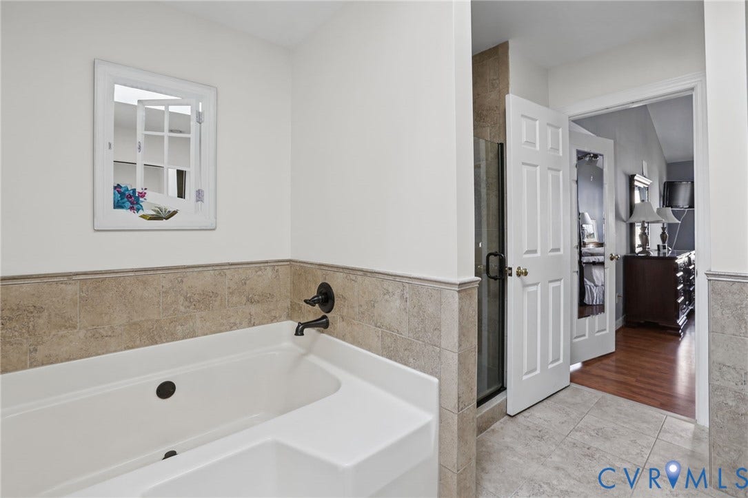 Soaking tub with a matte black faucet, tiled wainscoting, and large format tile flooring