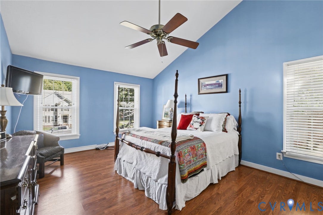 Vaulted ceiling, wood-look laminate flooring, ceiling fan, and multiple windows with blinds