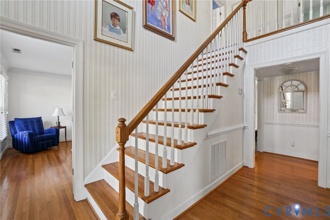 Hardwood flooring throughout, a classic staircase with wood-finish handrails and white balusters.