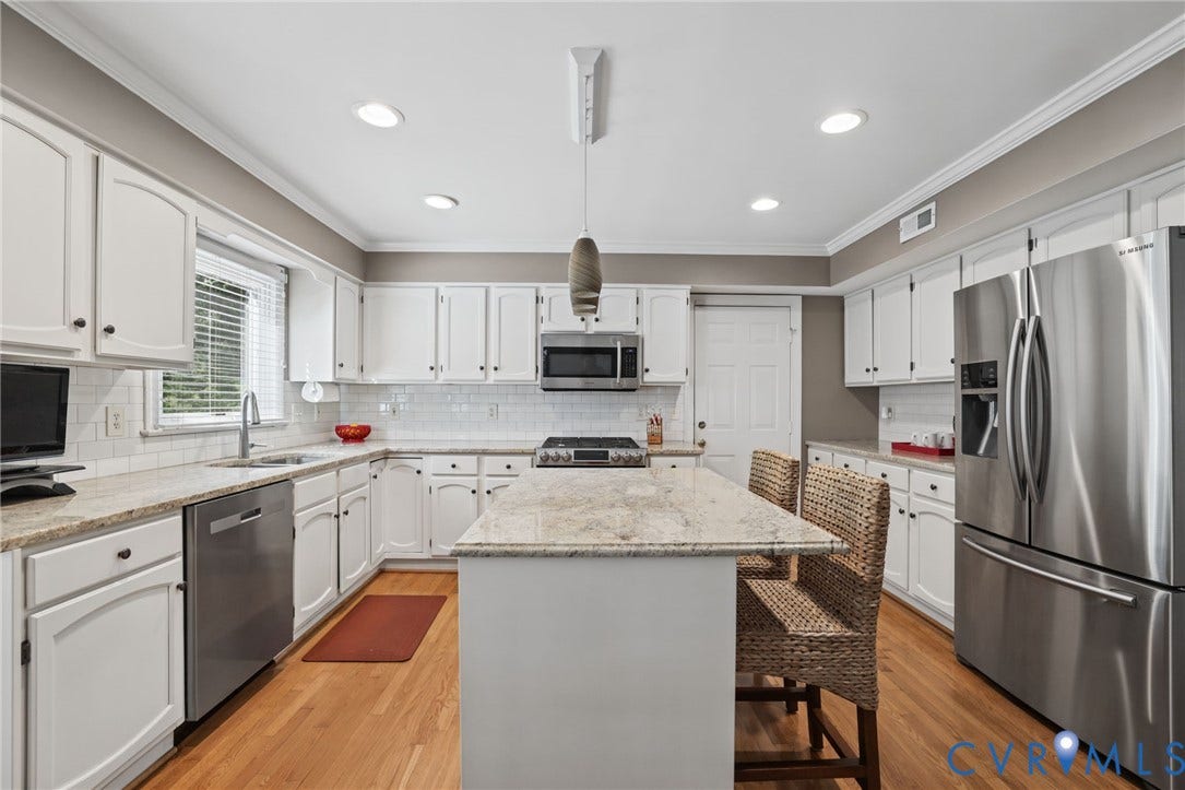 Well-appointed kitchen featuring an island with stone countertop, white cabinetry, stainless steel appliances, wood-finish flooring, and recessed lighting