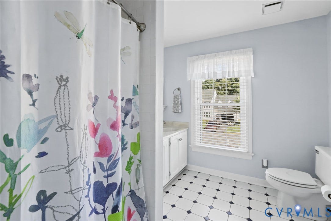 White tile flooring with black accents, light blue wall paint, window with blinds, white vanity with integrated sink, and a white toilet