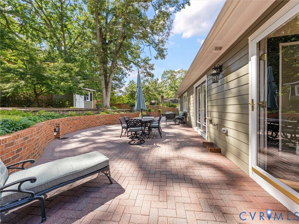 7723 Stuart Hall Road, Rollingwood Terrace, Henrico, VA 23229 Expansive brick paver patio featuring a curved brick retaining wall, exterior lighting fixtures, and multiple glass-paneled doors