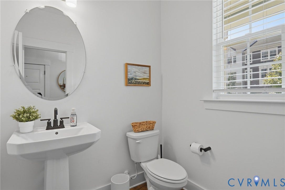 6142 Jackline Run, Watermark, Chesterfield, VA 23234 White pedestal sink with a matte black faucet, wall-mounted oval mirror, and a window with horizontal blinds