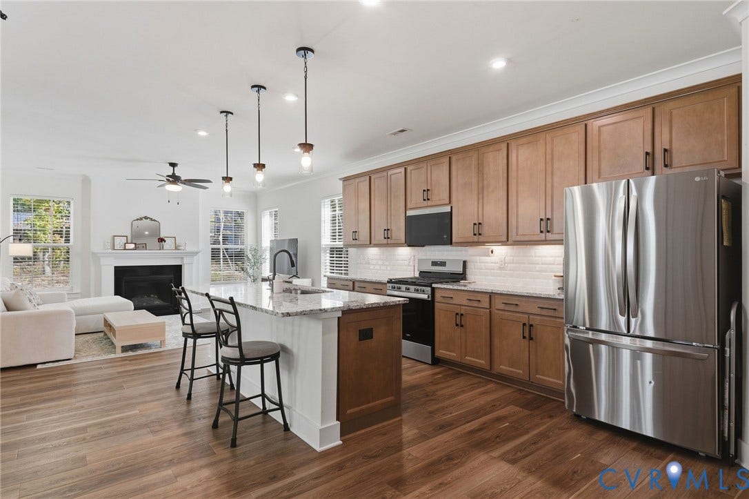6142 Jackline Run, Watermark, Chesterfield, VA 23234 Open-concept kitchen and living area featuring wood-finish flooring, a kitchen island with seating, pendant lighting, stainless steel appliances, and a fireplace