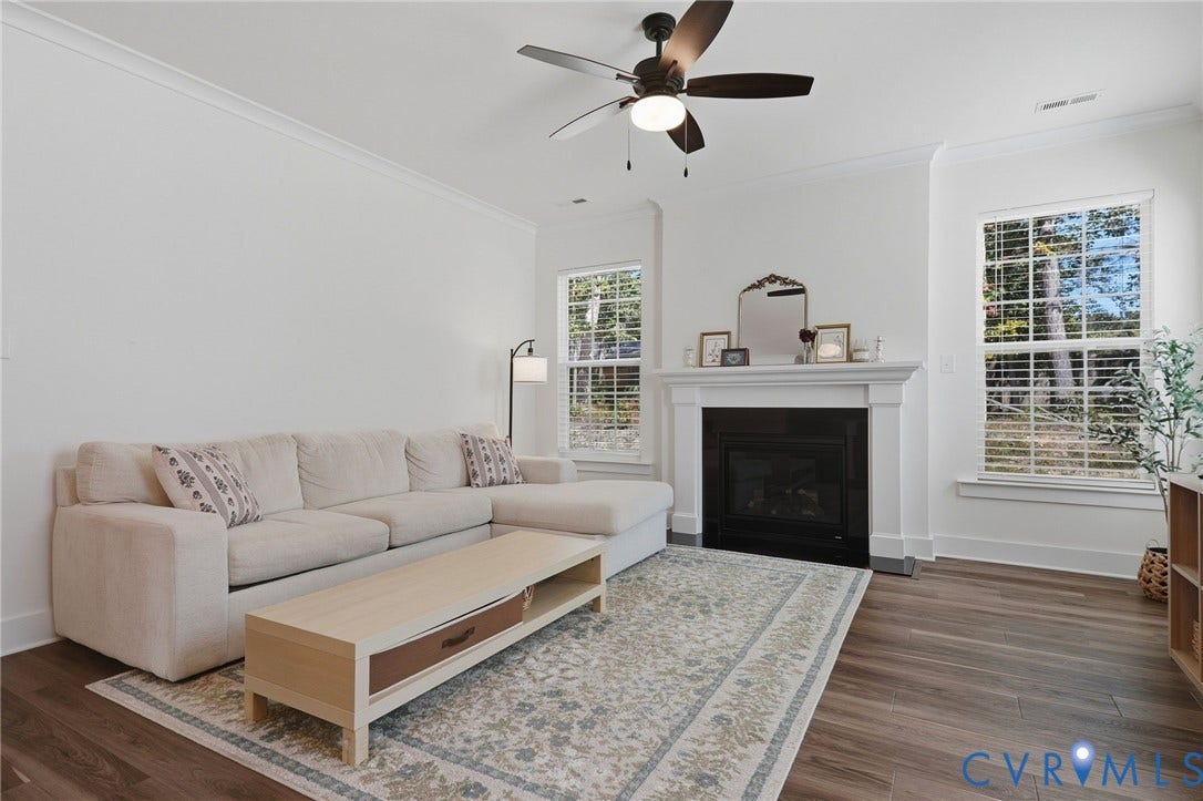 6142 Jackline Run, Watermark, Chesterfield, VA 23234 Living area featuring a ceiling fan, crown molding, wood-finish flooring, a fireplace with a white mantel, and multiple windows