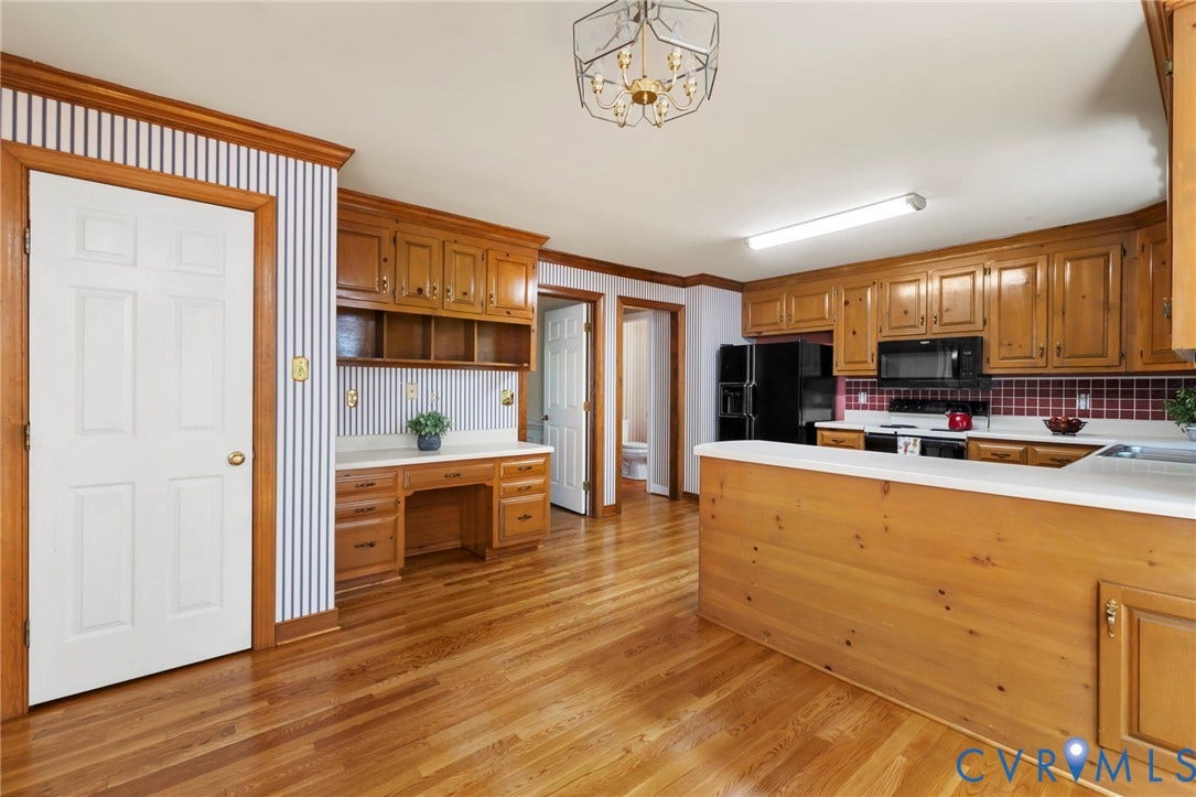Hardwood flooring throughout, built-in desk area with shelving, paneled doors, extensive wood cabinetry, and a kitchen island with white countertop
