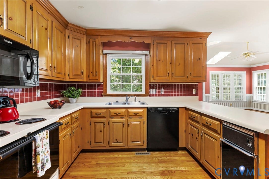 U-shaped kitchen with wood-finish cabinetry, light-toned countertops, and a red tiled backsplash