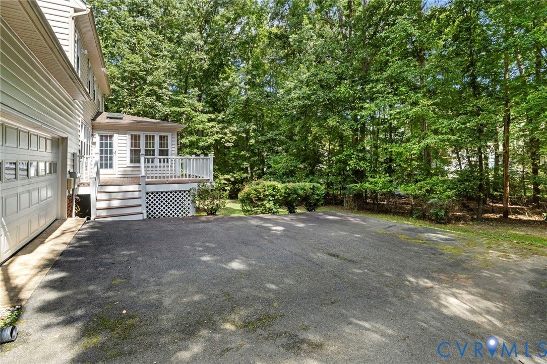Exterior siding, attached garage, wood deck with railing, French doors, and mature trees