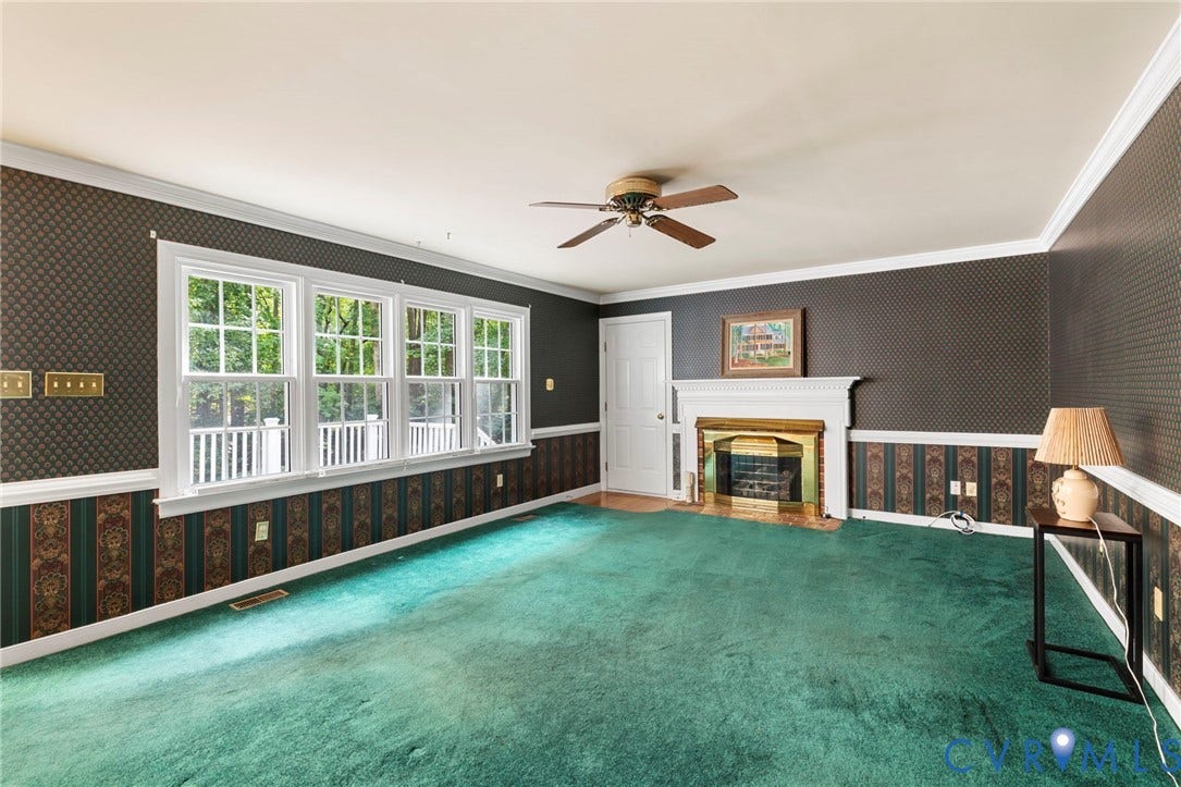 Fireplace with a white mantel and brass-toned screen, ceiling fan with wood-finish blades, white trim, white door, and multiple windows