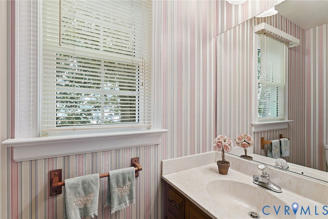 Vanity with a built-in sink and countertop, large wall-mounted mirror, and window with horizontal blinds
